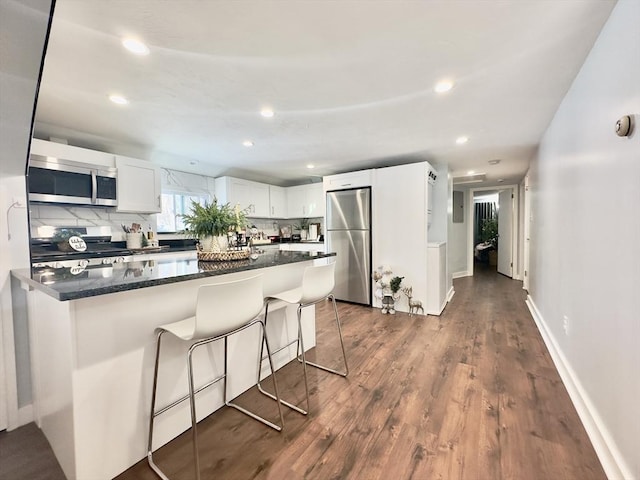 kitchen featuring a breakfast bar, white cabinets, decorative backsplash, stainless steel appliances, and dark wood-type flooring