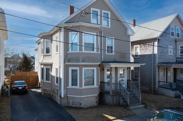 view of front of house with driveway, a chimney, and fence