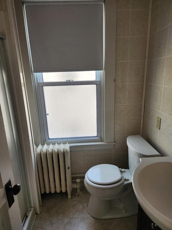 bathroom with tile patterned flooring, toilet, radiator heating unit, tile walls, and a sink