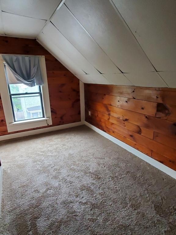 additional living space featuring wooden walls, carpet flooring, and vaulted ceiling