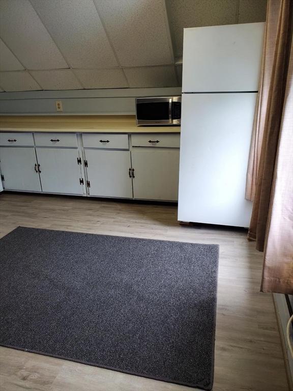 kitchen with wood finished floors, a drop ceiling, freestanding refrigerator, light countertops, and stainless steel microwave