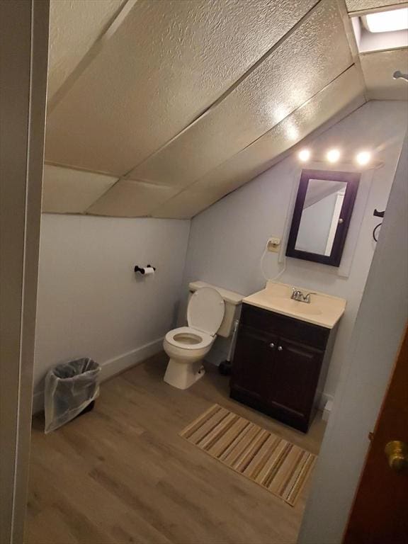 bathroom with vanity, wood finished floors, baseboards, lofted ceiling, and toilet