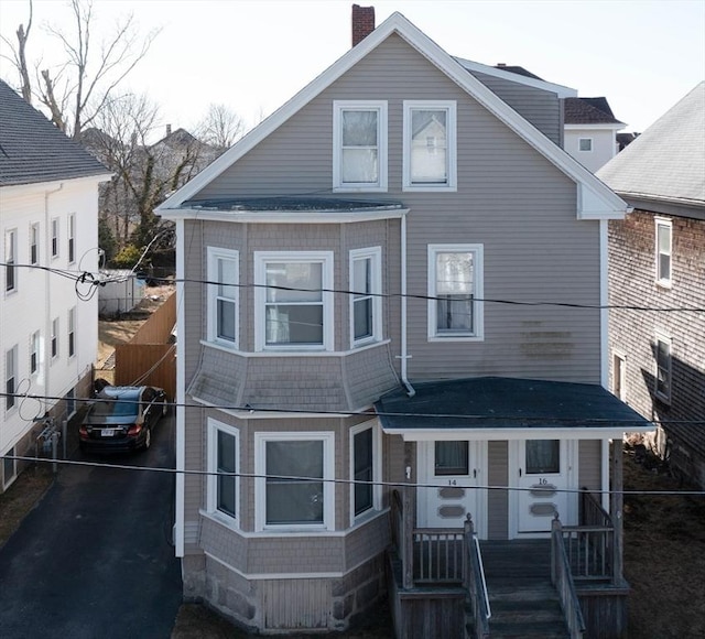 view of front facade featuring aphalt driveway, fence, and a chimney