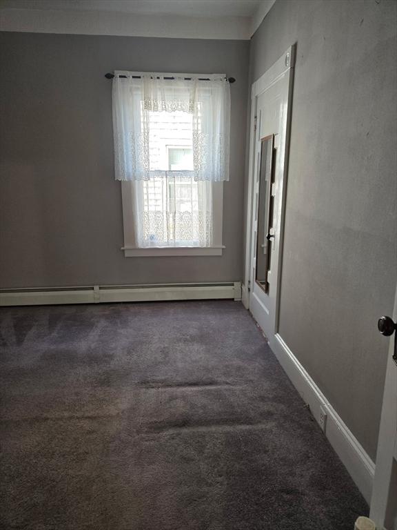 empty room featuring a baseboard heating unit, baseboards, and carpet floors