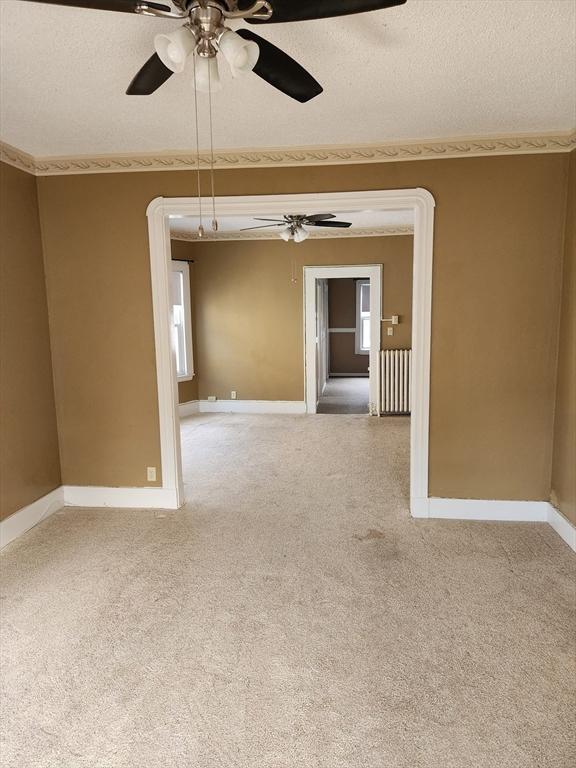 carpeted empty room featuring radiator, baseboards, and a textured ceiling