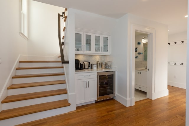 bar featuring sink, wine cooler, tasteful backsplash, white cabinetry, and light wood-type flooring