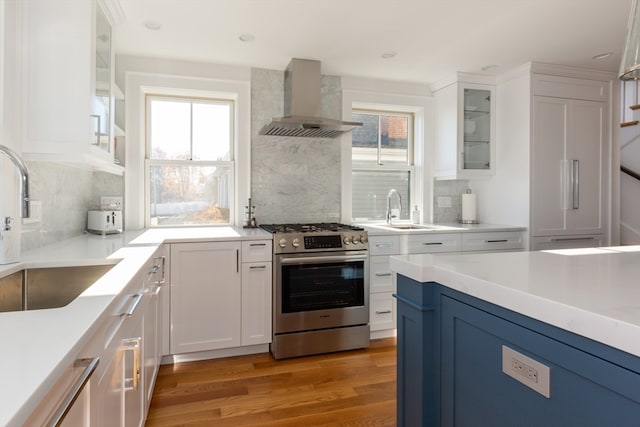 kitchen with white cabinets, backsplash, gas range, and wall chimney exhaust hood