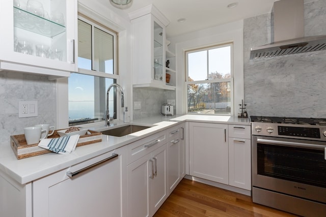 kitchen featuring wall chimney range hood, gas range, light hardwood / wood-style flooring, white cabinetry, and sink