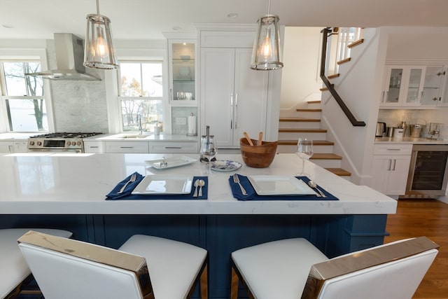 kitchen featuring backsplash, beverage cooler, a kitchen breakfast bar, and wall chimney exhaust hood