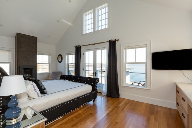 bedroom with high vaulted ceiling, light hardwood / wood-style floors, and a large fireplace