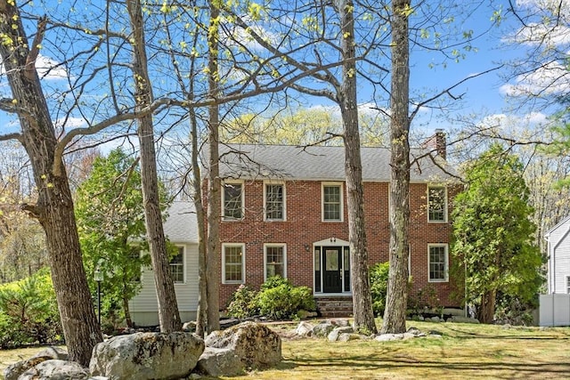 colonial house featuring brick siding, a chimney, and a front yard