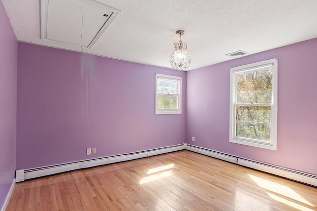 empty room with baseboard heating, visible vents, wood finished floors, and attic access