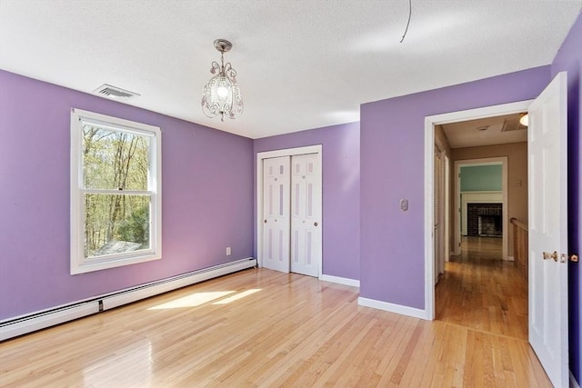 unfurnished bedroom featuring visible vents, baseboards, baseboard heating, light wood-type flooring, and a chandelier
