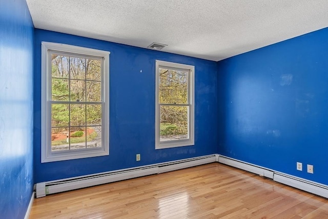 empty room featuring plenty of natural light, baseboard heating, a textured ceiling, and wood finished floors
