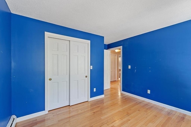 unfurnished bedroom featuring light wood finished floors, a textured ceiling, baseboards, a baseboard heating unit, and a closet