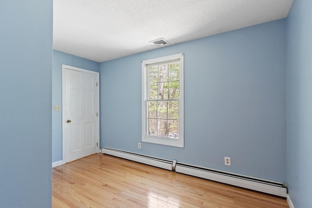 spare room featuring visible vents, wood finished floors, baseboards, a textured ceiling, and a baseboard heating unit