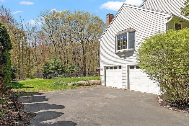 view of home's exterior featuring aphalt driveway, fence, a chimney, an attached garage, and a yard