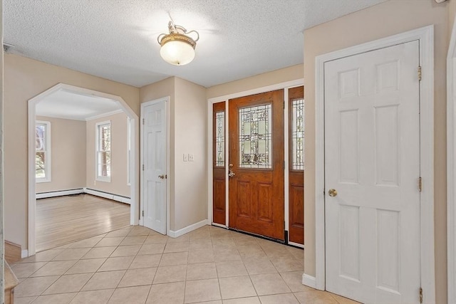 entryway with light tile patterned floors, arched walkways, baseboards, and a textured ceiling