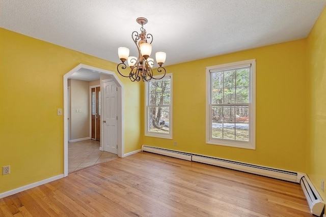 unfurnished dining area with wood finished floors, baseboards, a baseboard heating unit, a chandelier, and arched walkways