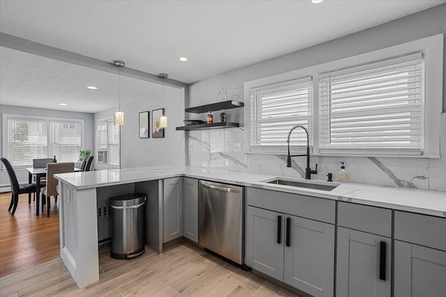 kitchen with a sink, stainless steel dishwasher, gray cabinets, light wood finished floors, and tasteful backsplash