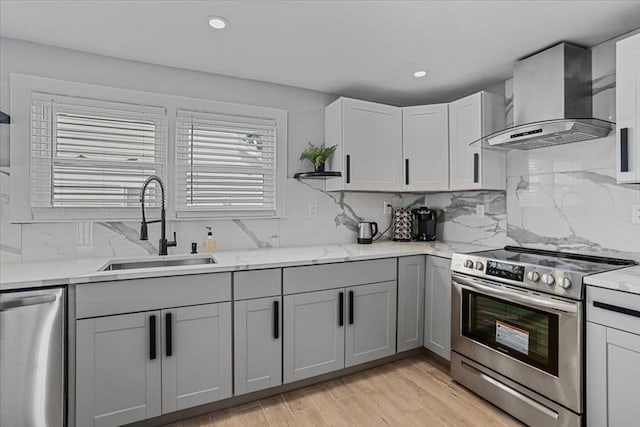 kitchen with tasteful backsplash, gray cabinetry, appliances with stainless steel finishes, a sink, and wall chimney exhaust hood