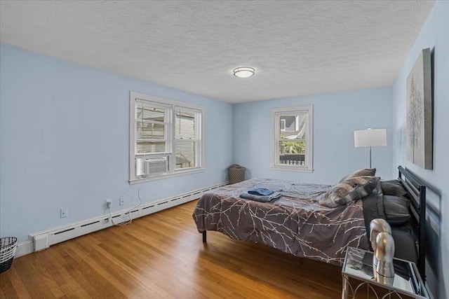 bedroom featuring a baseboard heating unit, multiple windows, a textured ceiling, and wood finished floors