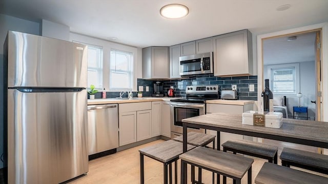 kitchen with tasteful backsplash, appliances with stainless steel finishes, gray cabinets, light countertops, and a sink