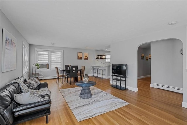 living area with baseboards, arched walkways, a baseboard radiator, wood finished floors, and cooling unit