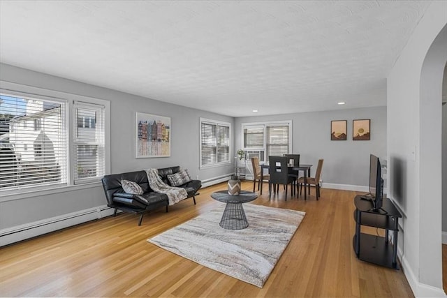 living room with arched walkways, light wood-type flooring, a wealth of natural light, and baseboards