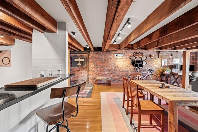 dining area featuring beamed ceiling, brick wall, and light wood-type flooring