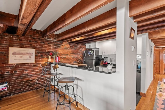 kitchen with white cabinetry, light hardwood / wood-style flooring, stainless steel refrigerator, kitchen peninsula, and brick wall