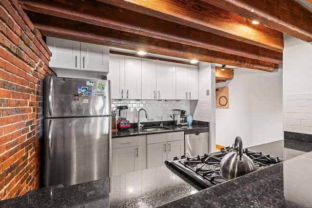 kitchen with sink, appliances with stainless steel finishes, white cabinetry, beam ceiling, and brick wall