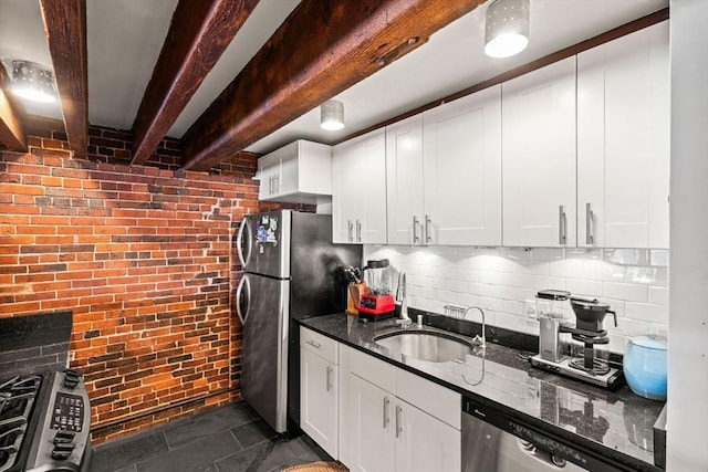 kitchen with brick wall, appliances with stainless steel finishes, white cabinetry, sink, and dark stone countertops