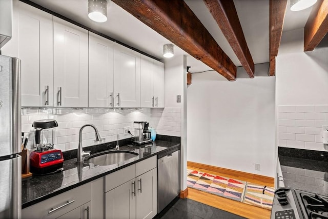 kitchen featuring sink, white cabinetry, stainless steel appliances, dark stone counters, and beamed ceiling