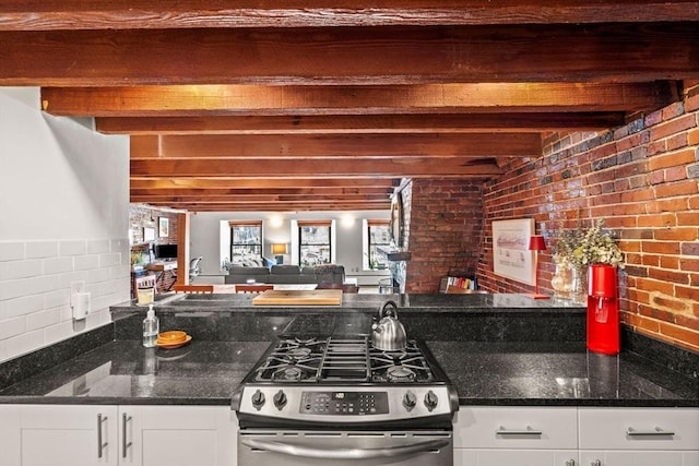 kitchen featuring white cabinetry, gas range, dark stone counters, and beamed ceiling