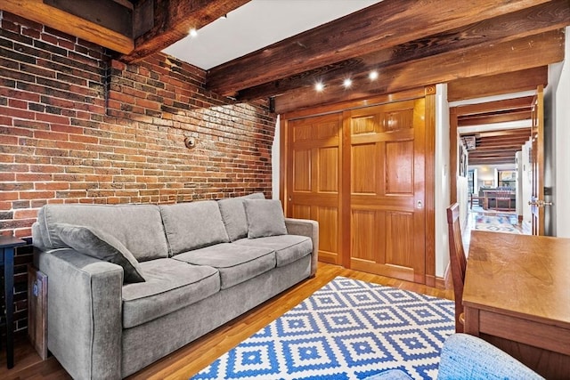 living room featuring wood-type flooring, beamed ceiling, and brick wall