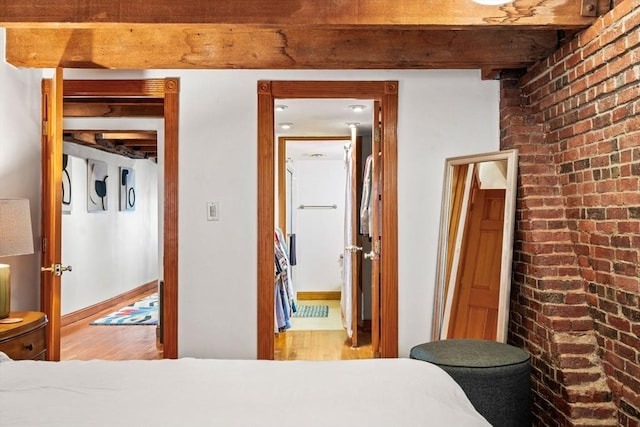 bedroom with beamed ceiling, brick wall, and light hardwood / wood-style flooring