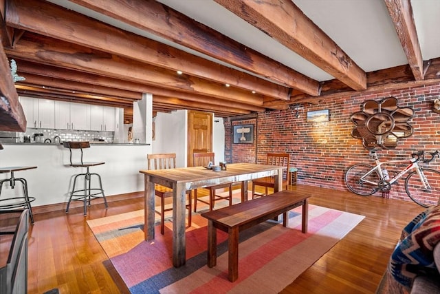 dining area featuring brick wall, beam ceiling, and light wood-type flooring