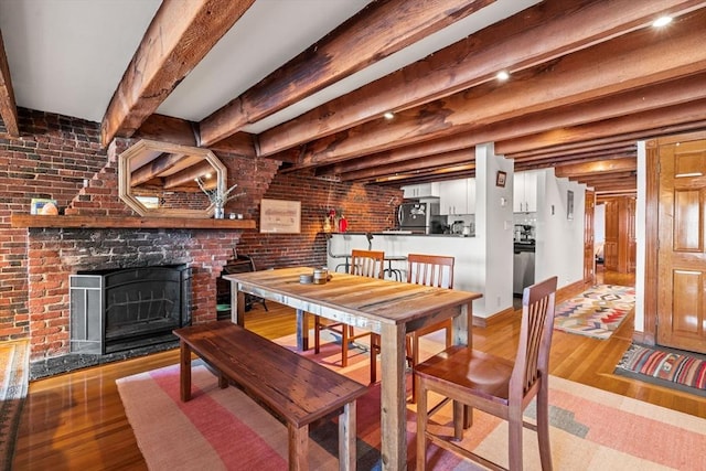 dining space with beamed ceiling, brick wall, a fireplace, and light hardwood / wood-style floors