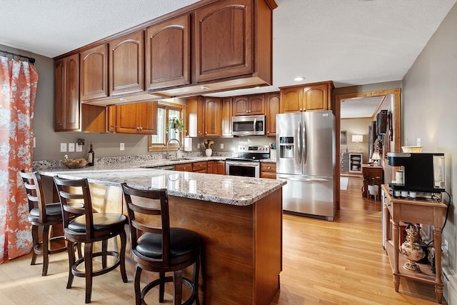 kitchen featuring sink, a breakfast bar, appliances with stainless steel finishes, light stone countertops, and kitchen peninsula