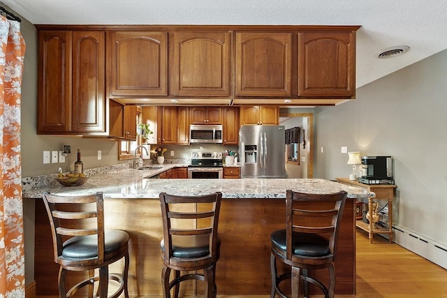 kitchen featuring stainless steel appliances, light stone counters, a kitchen bar, kitchen peninsula, and light wood-type flooring