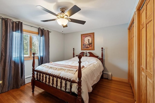 bedroom featuring wood-type flooring, a baseboard heating unit, ceiling fan, and a closet