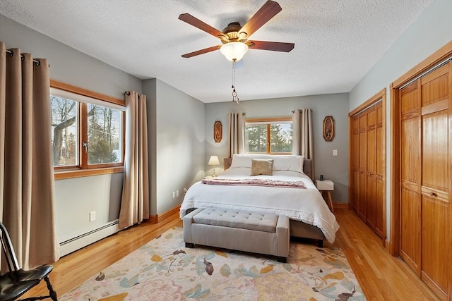 bedroom with ceiling fan, baseboard heating, multiple closets, a textured ceiling, and light hardwood / wood-style flooring