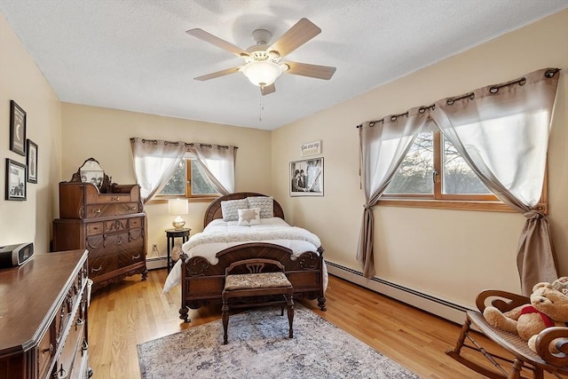 bedroom with baseboard heating, ceiling fan, light hardwood / wood-style flooring, and a textured ceiling