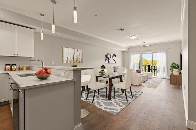 kitchen with crown molding, pendant lighting, white cabinetry, and hardwood / wood-style flooring