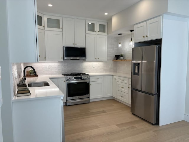 kitchen featuring stainless steel appliances, a sink, light wood-style floors, light countertops, and decorative backsplash