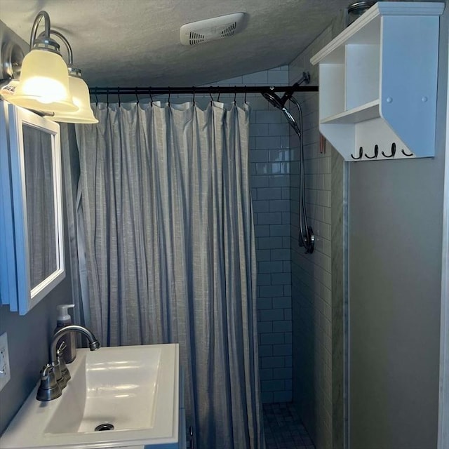 bathroom with a textured ceiling, tiled shower, visible vents, and a sink