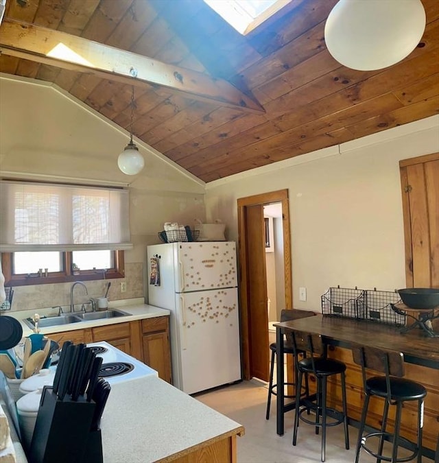 kitchen featuring vaulted ceiling, brown cabinetry, freestanding refrigerator, and a sink