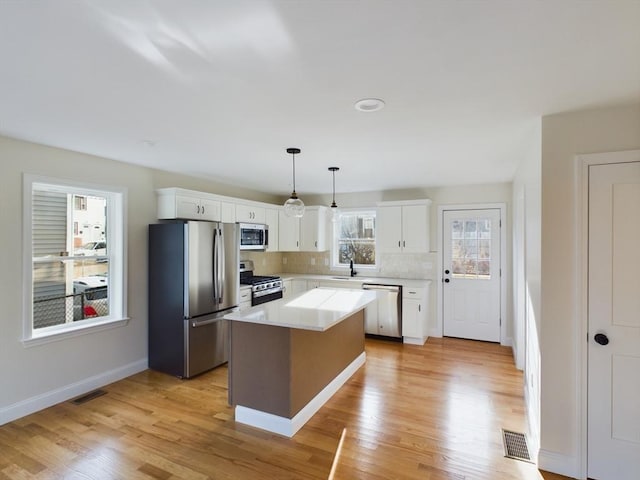 kitchen featuring pendant lighting, appliances with stainless steel finishes, a kitchen island, white cabinetry, and backsplash