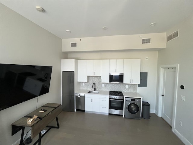kitchen with appliances with stainless steel finishes, washer / clothes dryer, a sink, decorative backsplash, and white cabinetry